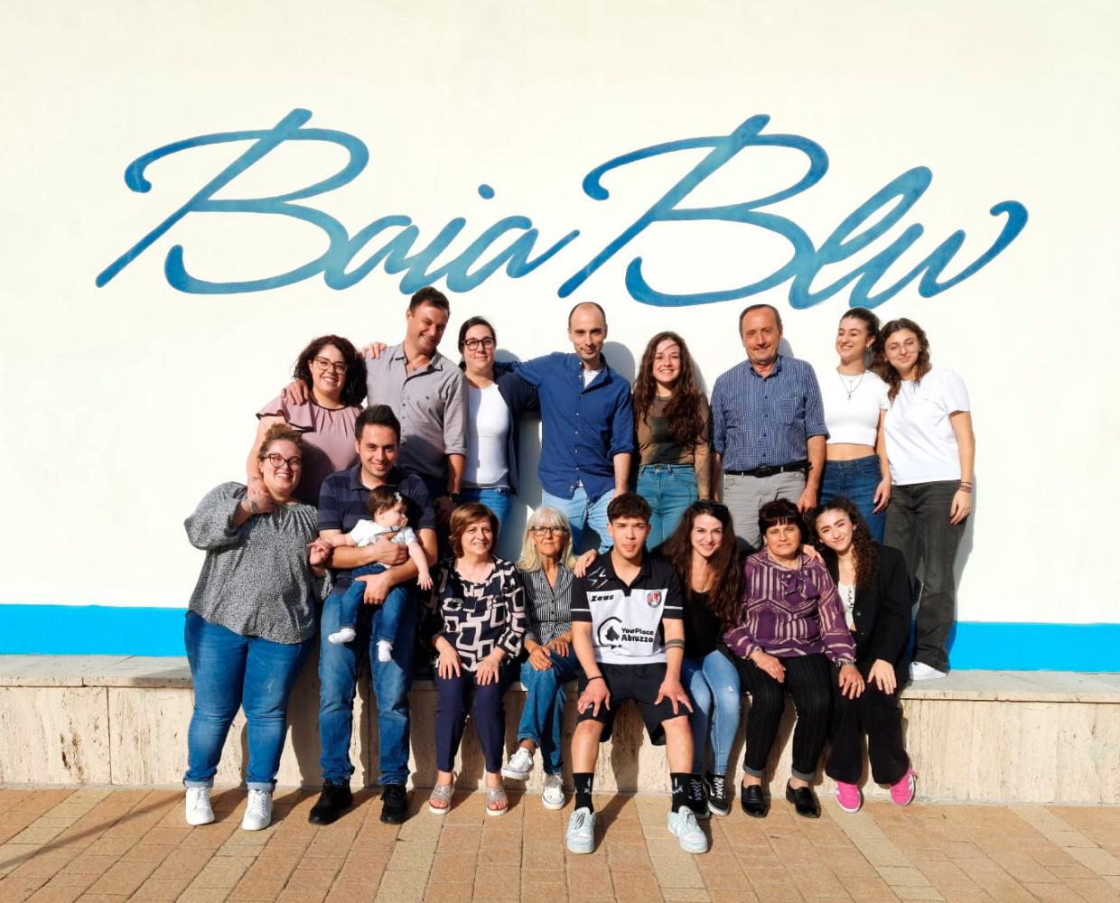 Gruppo di persone sorridenti davanti a un muro con scritta Baia Blu.